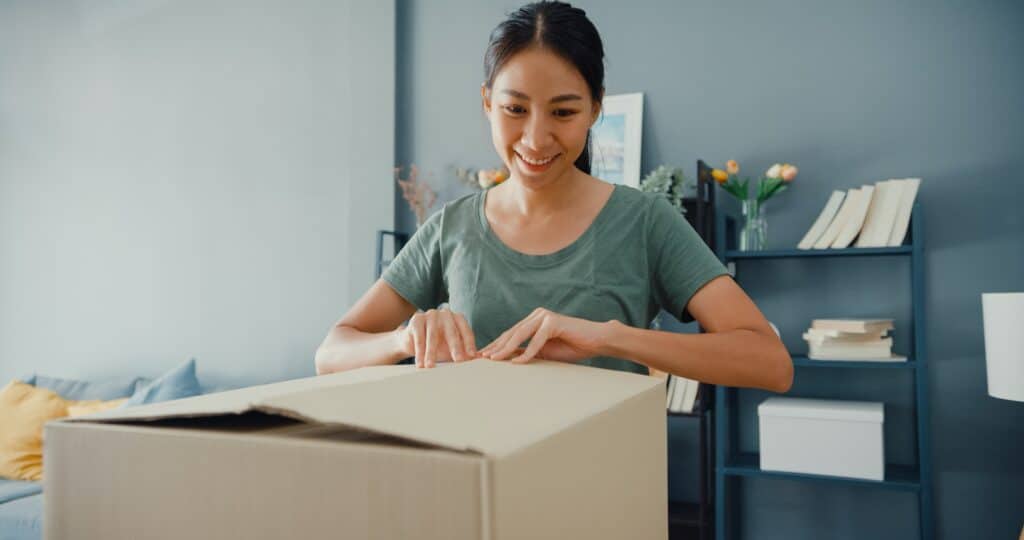 sia lady unboxing cardboard delivery package from online marketplace in living room.